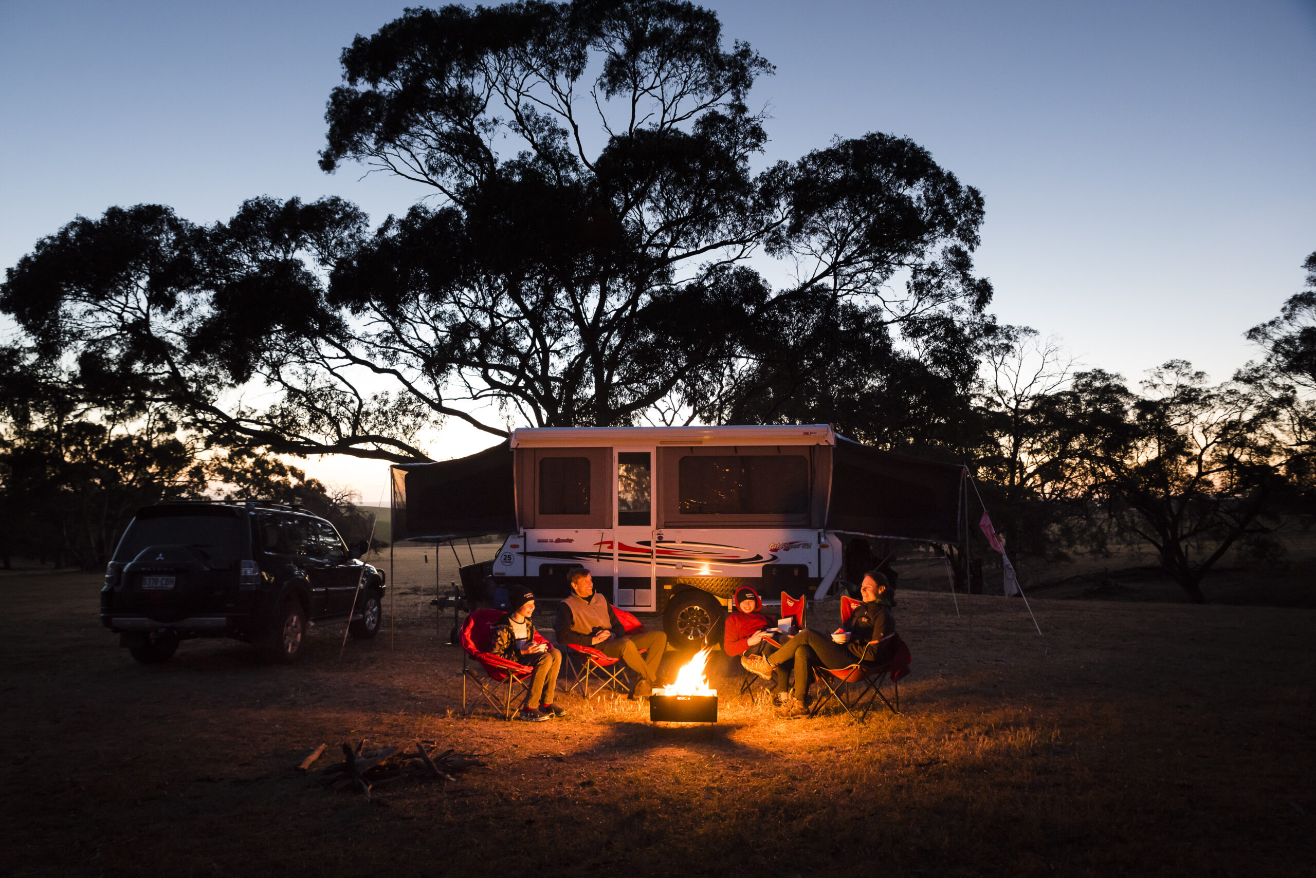 Campers sit around a campfire as the sun sets.
